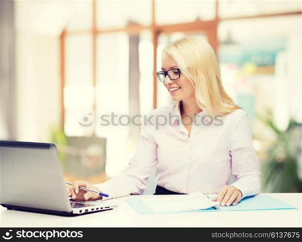 education, business and technology concept - smiling businesswoman or student in eyeglasses with laptop computer and documents over office room background