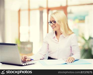 education, business and technology concept - smiling businesswoman or student in eyeglasses with laptop computer and documents over office room background