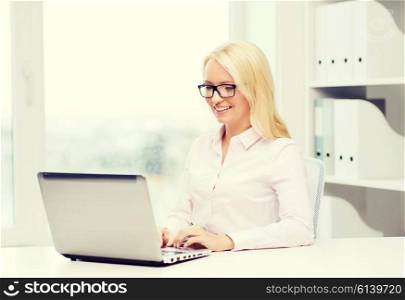 education, business and technology concept - smiling businesswoman or student in eyeglasses with laptop computer in office