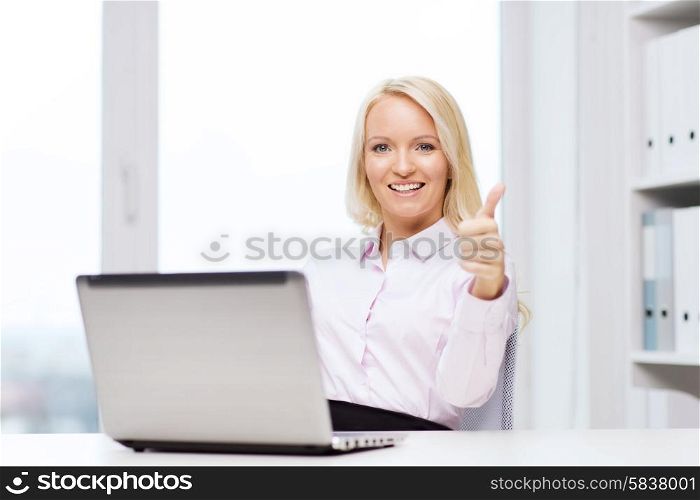 education, business and technology concept - smiling businesswoman or student showing thumbs up with laptop computer in office