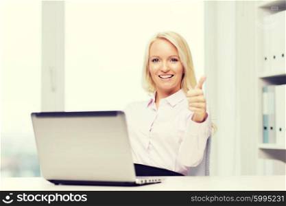 education, business and technology concept - smiling businesswoman or student showing thumbs up with laptop computer in office