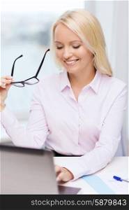 education, business and technology concept - smiling businesswoman or student with eyeglasses and laptop computer in office