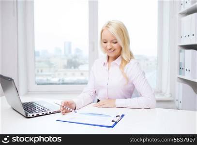education, business and technology concept - smiling businesswoman or student with laptop computer and papers sitting in office