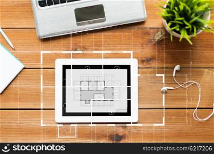 education, business, architecture and technology concept - close up of tablet pc computer, laptop and earphones on wooden table with blueprint projection