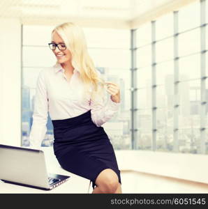 education, business, flirting and technology concept - smiling businesswoman or secretary with laptop computer sitting on table over office room with city view window background