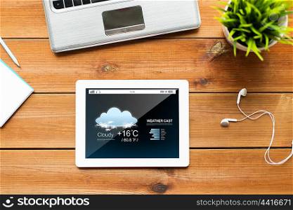 education, business, forecast and technology concept - close up of tablet pc computer, laptop and earphones on wooden table with weather cast