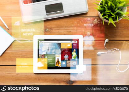 education, business, mass media and technology concept - close up of tablet pc computer, laptop and earphones on wooden table with internet application on screen