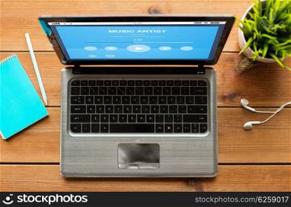 education, business, multimedia and technology concept - close up of laptop computer with music player on screen on wooden table