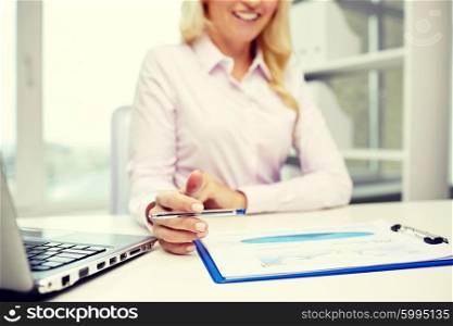 education, business, people and technology concept - close up of smiling businesswoman with laptop computer and papers sitting in office