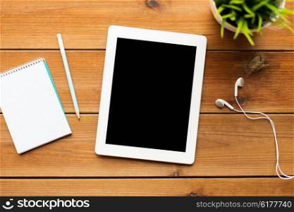 education, business, people and technology concept - close up of tablet pc computer, notebook with pencil and earphones on wooden table