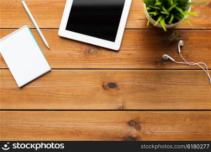 education, business, people and technology concept - close up of tablet pc computer, notebook with pencil and earphones on wooden table