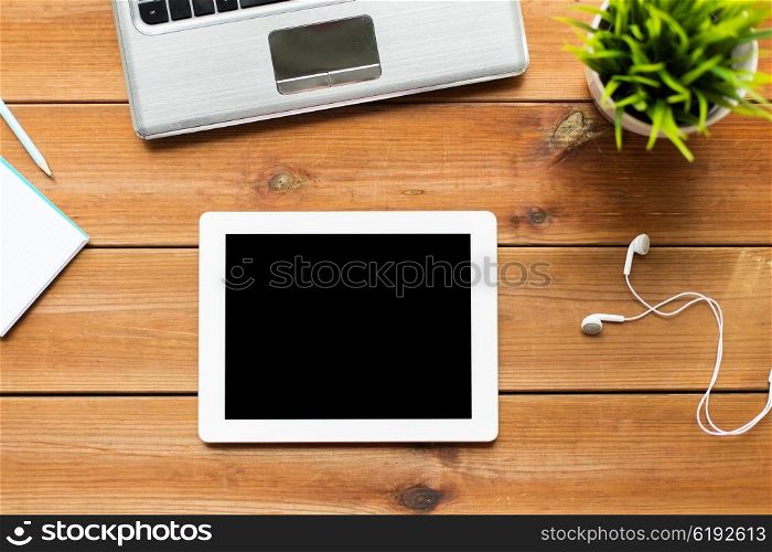 education, business, people and technology concept - close up of tablet pc computer, laptop and earphones on wooden table