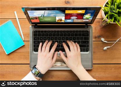 education, business, people and technology concept - close up of woman or student typing on laptop computer with internet news on screen, notebook and earphones on wooden table