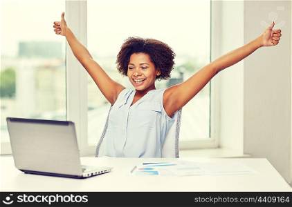 education, business, success, gesture and technology concept - happy african american businesswoman or student with laptop computer and papers showing thumbs up and celebrating triumph at office