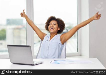 education, business, success, gesture and technology concept - happy african american businesswoman or student with laptop computer and papers showing thumbs up and celebrating triumph at office