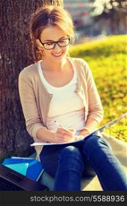 education, campus and people concept - smiling teenager in eyeglasses writing in notebook