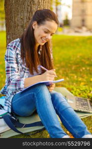 education, campus and people concept - smiling teenager writing in notebook