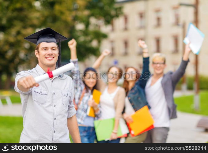 education, campus and teenage concept - smiling teenage boy in corner-cap with diploma and classmates on the back