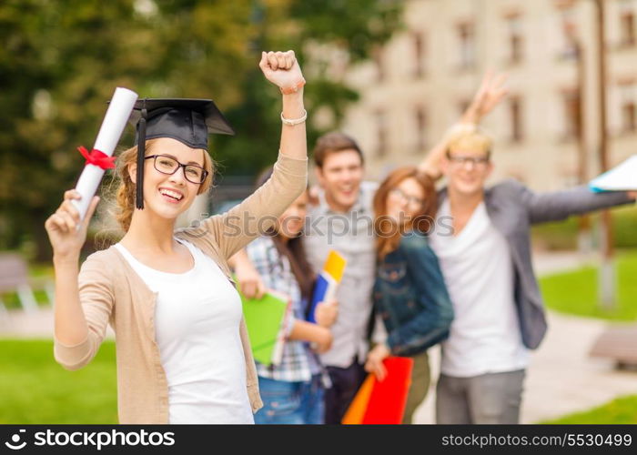 education, campus and teenage concept - smiling teenage girl in corner-cap and eyeglasses with diploma and classmates on the back