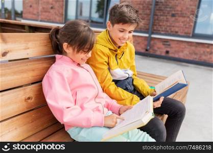 education, childhood and people concept - happy school children or brother and sister reading books sitting on wooden street bench outdoors. school children reading books sitting on bench