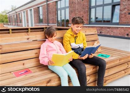 education, childhood and people concept - happy school children or brother and sister reading books sitting on wooden street bench outdoors. school children reading books sitting on bench