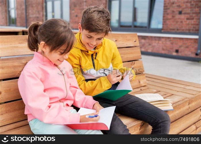 education, childhood and people concept - happy school children or brother and sister with notebooks and books sitting on wooden street bench outdoors. school children with notebooks sitting on bench