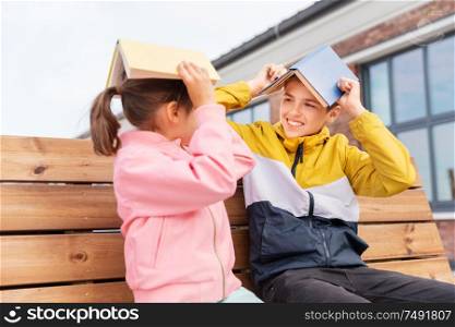 education, childhood and people concept - happy school children or brother and sister with books sitting on wooden street bench outdoors and having fun. school children with books having fun outdoors