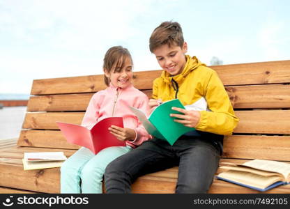 education, childhood and people concept - happy school children or brother and sister with notebooks and books sitting on wooden street bench outdoors. school children with notebooks sitting on bench
