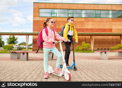 education, childhood and people concept - happy school children with backpacks and scooters outdoors. happy school children with backpacks and scooters