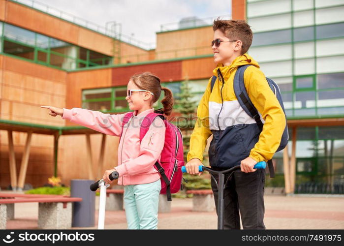 education, childhood and people concept - happy school children with backpacks and scooters outdoors. happy school children with backpacks and scooters