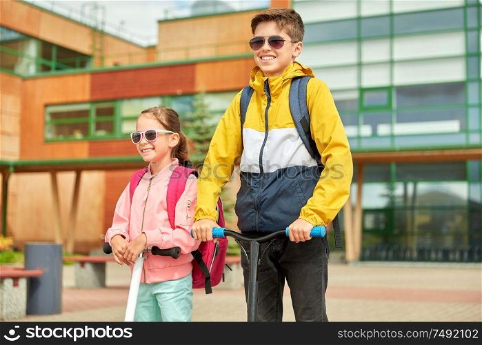 education, childhood and people concept - happy school children with backpacks and scooters outdoors. happy school children with backpacks and scooters