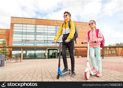 education, childhood and people concept - happy school children with backpacks and scooters outdoors. happy school children with backpacks and scooters