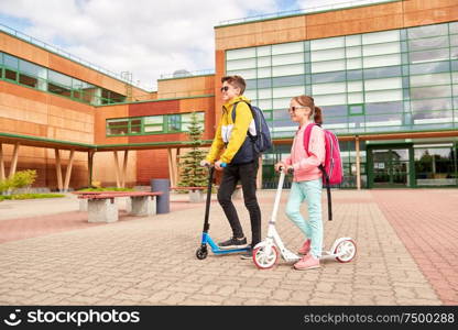 education, childhood and people concept - happy school children with backpacks and scooters outdoors. happy school children with backpacks and scooters