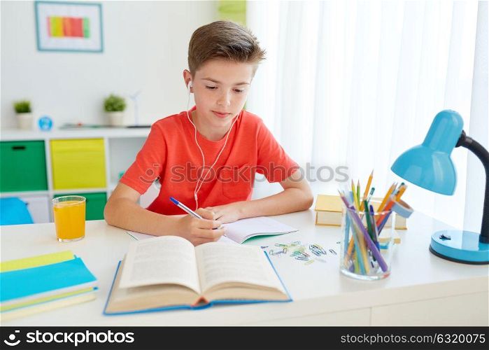 education, childhood and people concept - happy student boy in earphones writing to notebook from book at home. student boy in earphones writing to notebook