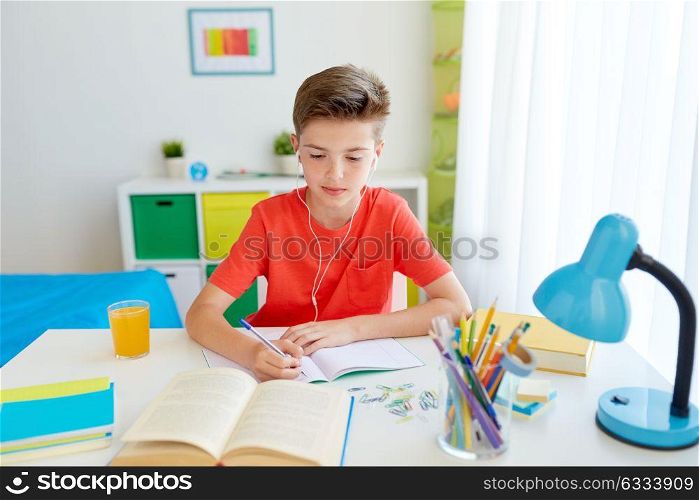 education, childhood and people concept - happy student boy in earphones writing to notebook from book at home. student boy in earphones writing to notebook