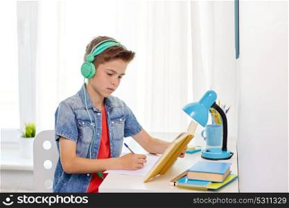 education, childhood and people concept - happy student boy in headphones writing to notebook from book at home. student boy in headphones writing to notebook