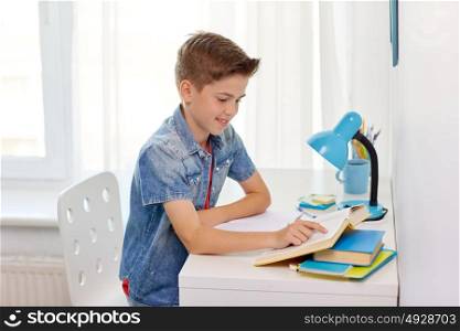 education, childhood and people concept - happy student boy reading book at home. student boy reading book at home table
