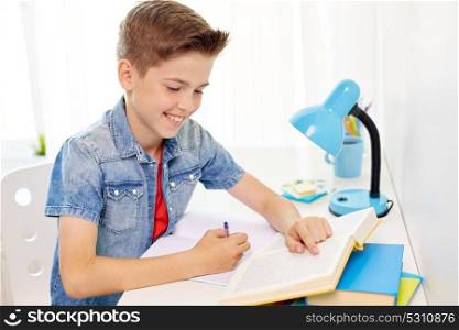 education, childhood and people concept - happy student boy with book writing to notebook at home. student boy with book writing to notebook at home