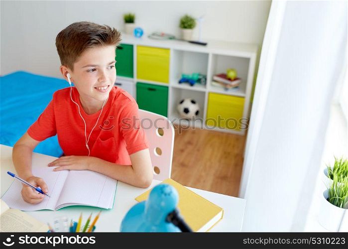 education, childhood and people concept - happy student boy with earphones writing to notebook at home. happy student boy writing to notebook at home