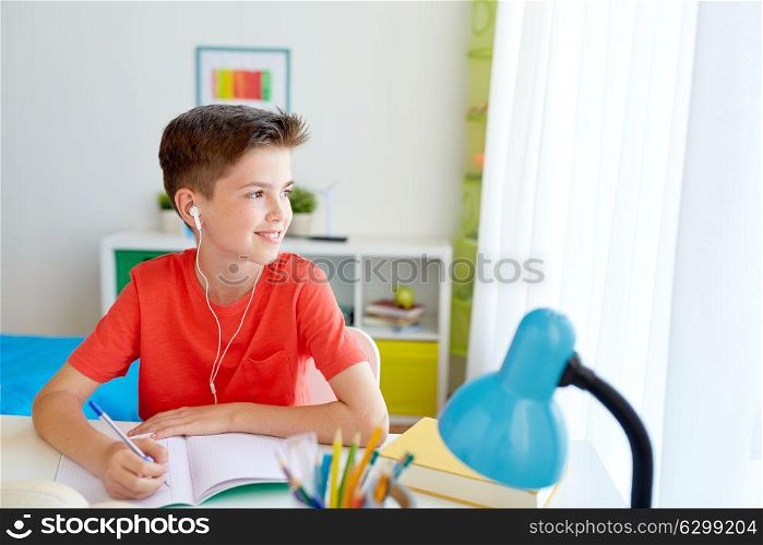 education, childhood and people concept - happy student boy with earphones writing to notebook at home. happy student boy writing to notebook at home