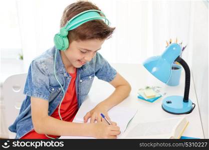 education, childhood and people concept - happy student boy with headphones writing to notebook at home. student boy in headphones writing to notebook