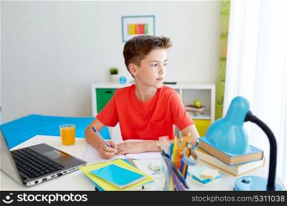 education, childhood and people concept - happy student boy with laptop computer writing to notebook at home. student boy with laptop writing to notebook