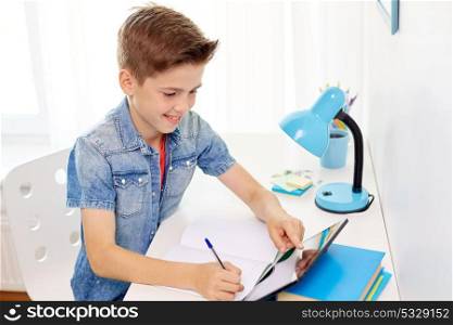 education, childhood and people concept - happy student boy with tablet pc computer writing to notebook at home. student boy with tablet pc writing to notebook