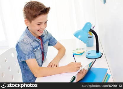 education, childhood and people concept - happy student boy with tablet pc computer writing to notebook at home. student boy with tablet pc writing to notebook