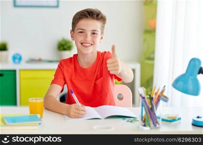 education, childhood and people concept - happy student boy writing to notebook at home and showing thumbs up. happy student boy writing to notebook at home