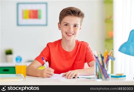 education, childhood and people concept - happy student boy writing to notebook at home. happy student boy writing to notebook at home