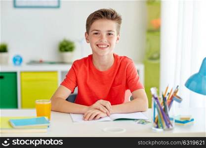 education, childhood and people concept - happy student boy writing to notebook at home. happy student boy writing to notebook at home