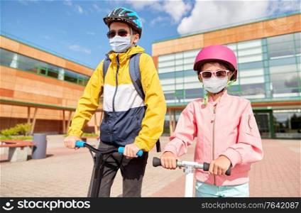education, childhood and people concept - school children in face protective medical mask for protection from virus disease riding scooters outdoors. children in masks riding scooters over school