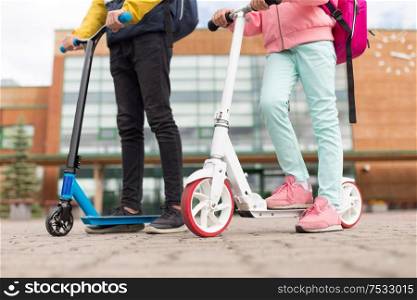 education, childhood and people concept - school children with backpacks and scooters outdoors. school children with backpacks and scooters