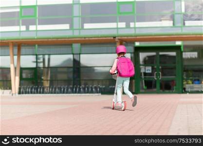 education, childhood and people concept - school girl with backpack riding scooter. school girl with backpack riding scooter